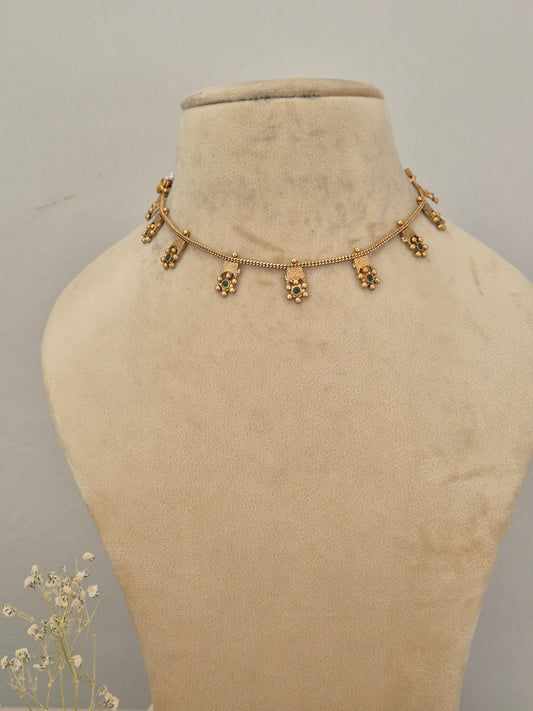 Gold-toned traditional choker necklace featuring a delicate beaded chain with dangling green stone and tiny floral clusters by naitri.in