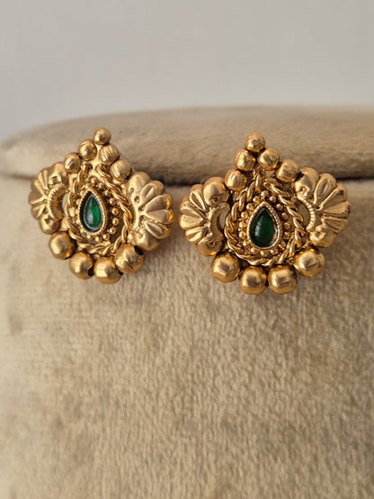 A pair of ornate gold-toned traditional earrings with green teardrop-shaped stone centers, by naitri.in