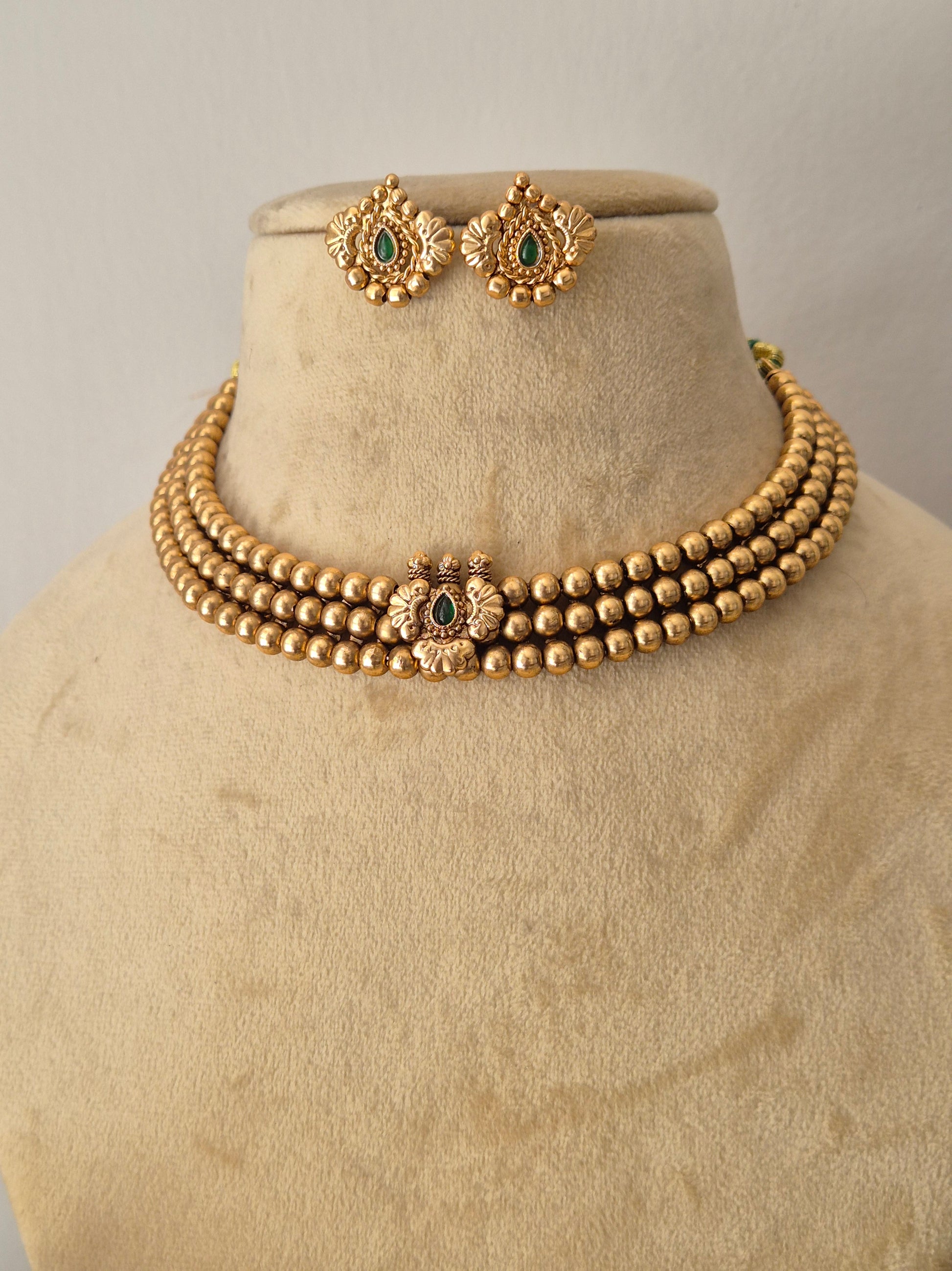 A gold-toned traditional jewelry set, featuring a beaded bracelet with ornate floral motifs and matching earrings with green stone accents for festive wear by naitri.in