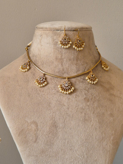 Traditional Indian gold-tone necklace set displayed on a cream jewelry bust, featuring white stones and pearl bead accents by naitri.in