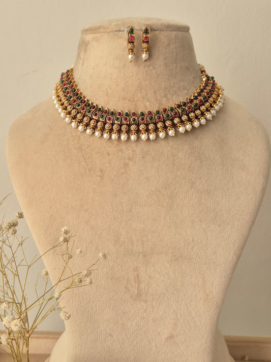 Necklace and earrings set An ornate gold-plated choker featuring ruby-red stones ,emerald-green stone sand delicate pearl attached with matching earrings by naitri.in