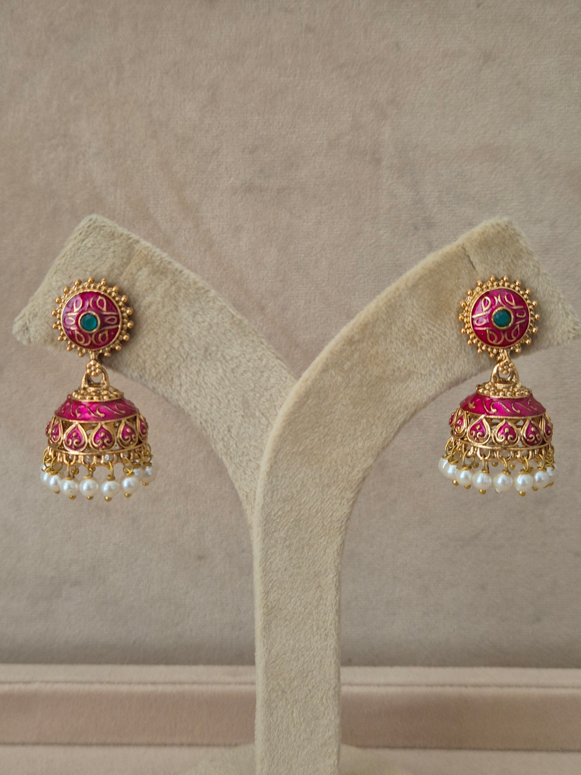 Close-up of Naitri Rakshita premium gold ethnic earrings showcasing traditional Indian Jhumka craftsmanship with intricate pink and green floral enamel accents and delicate pearl dangling beads. by naitri.in