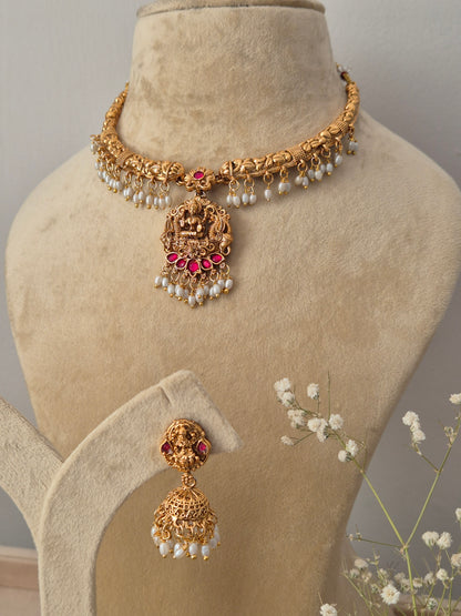 Gold-polished brass choker with a Lakshmi pendant, ruby-red stones, hanging pearls, and coordinating drop earrings by naitri.in