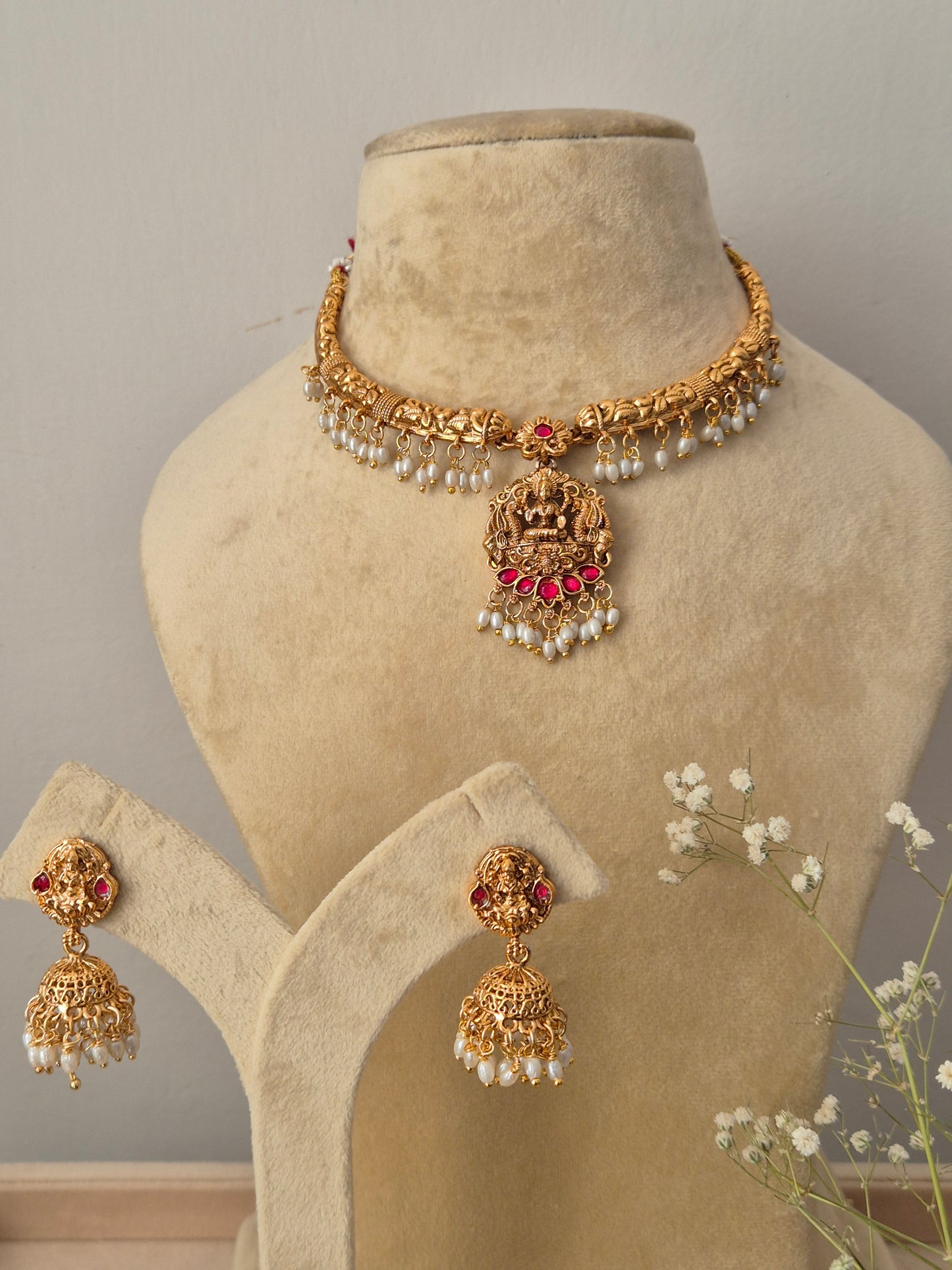 Handcrafted traditional gold-plated temple jewelry choker necklace featuring a central Goddess Lakshmi motif pendant with ruby-red stone accents and dangling white pearls, paired with matching jhumka earrings by naitri.in