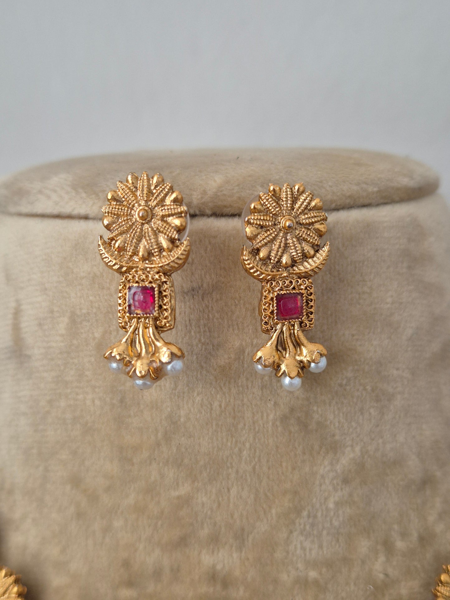 Antique gold earrings earrings and small red gemstones intricate textured circular engravings, small red stone embellishments, and delicate white hanging pearls by naitri.in