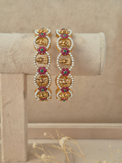 Set of 2 gold-plated bangles featuring oval-shaped motifs studded with green and pink gemstones surrounded by tiny white pearls by naitri.in