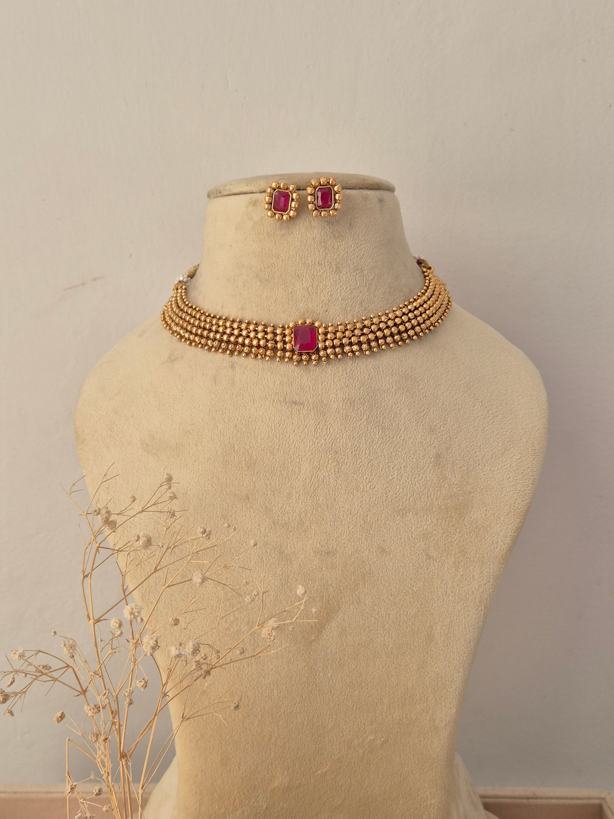 Traditional gold-plated choker necklace set featuring a vibrant pink center stone, displayed on a mannequin with matching stud earrings by Naitri