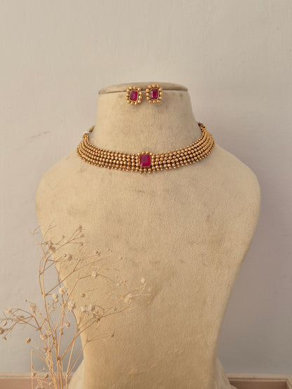 Traditional gold-plated choker necklace set featuring a vibrant pink center stone, displayed on a mannequin with matching stud earrings by Naitri