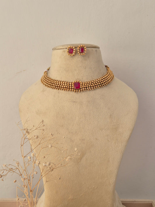 Traditional gold-plated choker necklace set featuring a vibrant pink center stone, displayed on a mannequin with matching stud earrings by Naitri