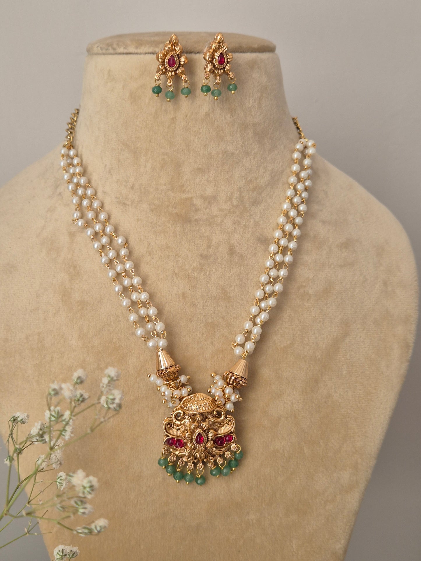 Handcrafted dual-strand pearl necklace featuring a detailed gold-tone brass alloy pendant with red and green stones and small emerald-colored bead drops by naitri.in