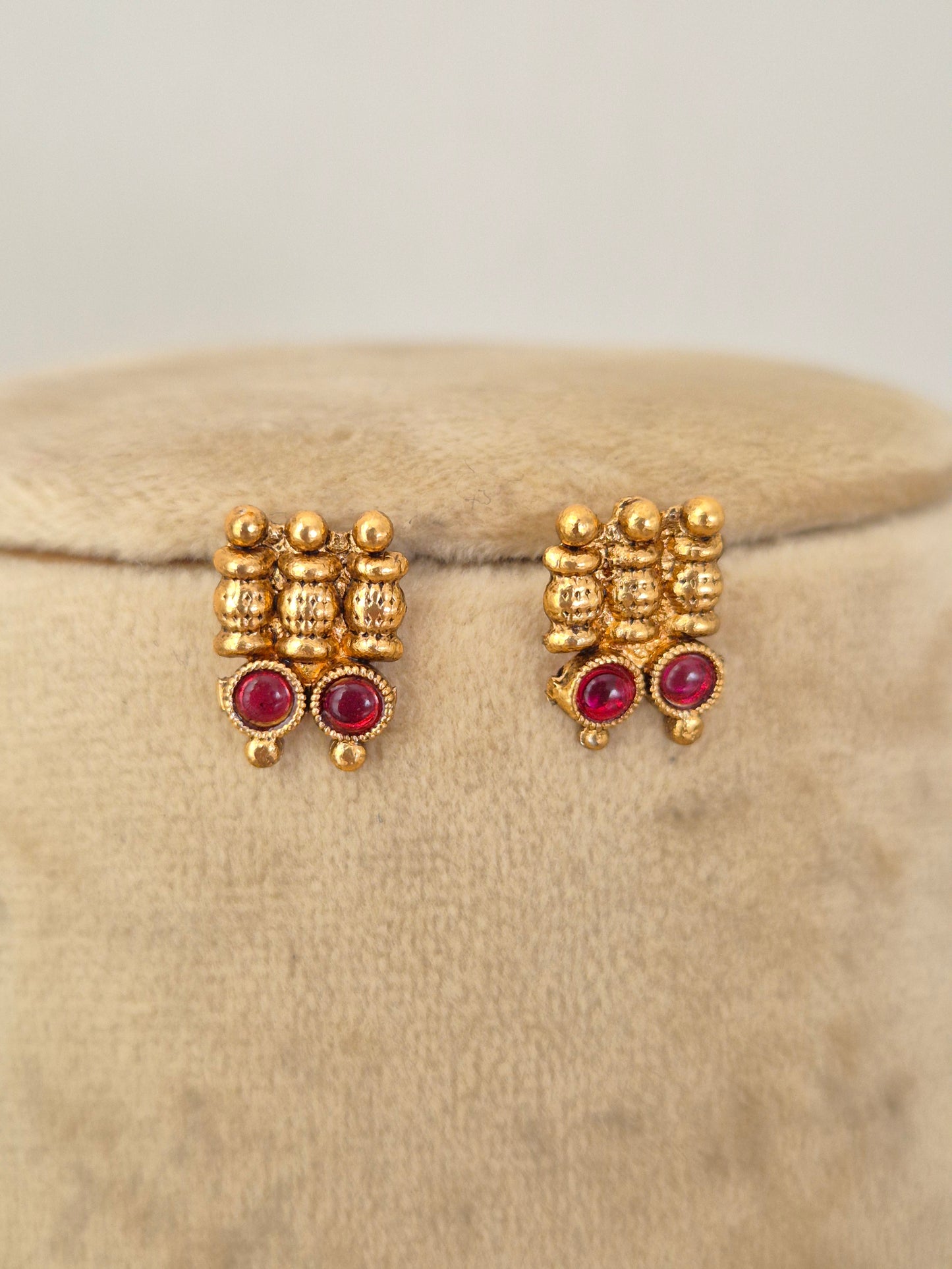 A pair of gold-toned traditional stud earrings with small clear stones and round red gemstones, by naitri.in