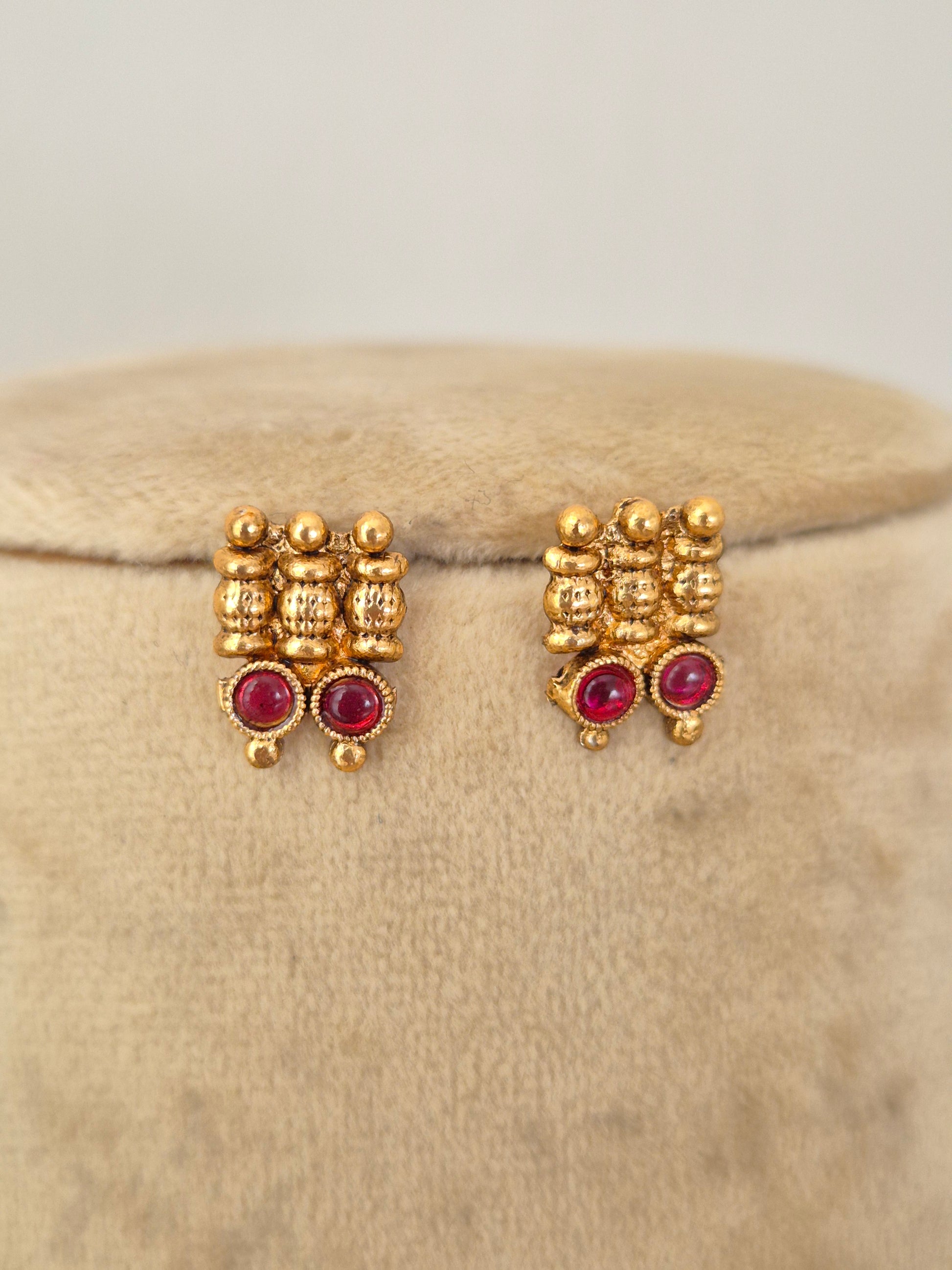 A pair of gold-toned traditional stud earrings with small clear stones and round red gemstones, by naitri.in