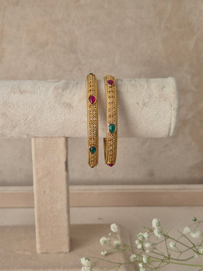 Two gold-plated bangles with intricate filigree work and small colored gemstone accents, by naitri.in