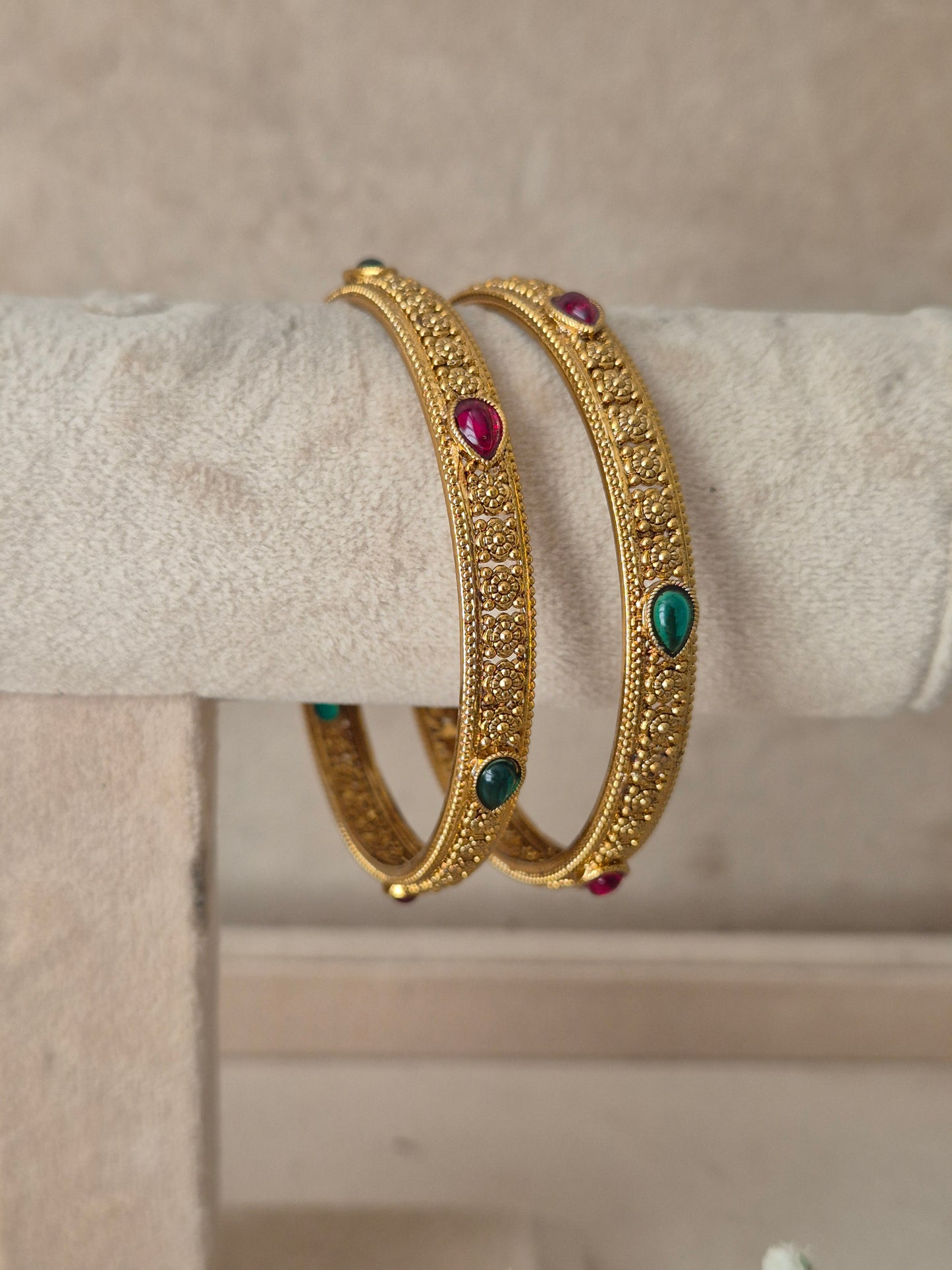 Two gold-toned filigree bangles with small clear stones and teardrop-shaped green and pink gemstone accents, by naitri.in
