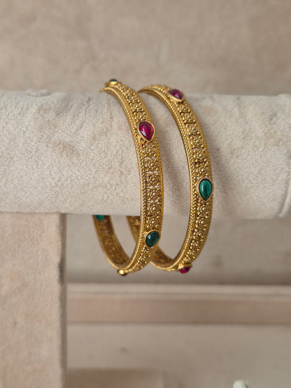 Two gold-toned filigree bangles with small clear stones and teardrop-shaped green and pink gemstone accents, by naitri.in