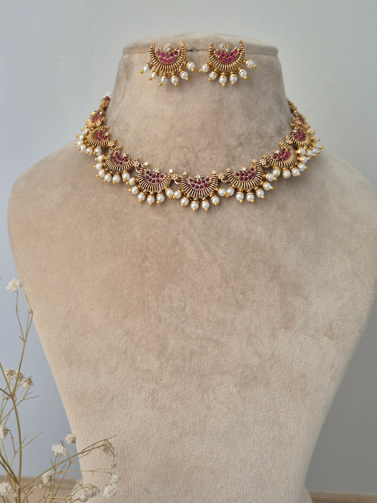 Gold jewelry design half-moon with small red stones in middle and pearls attached outside and same design earrings by naitri.in