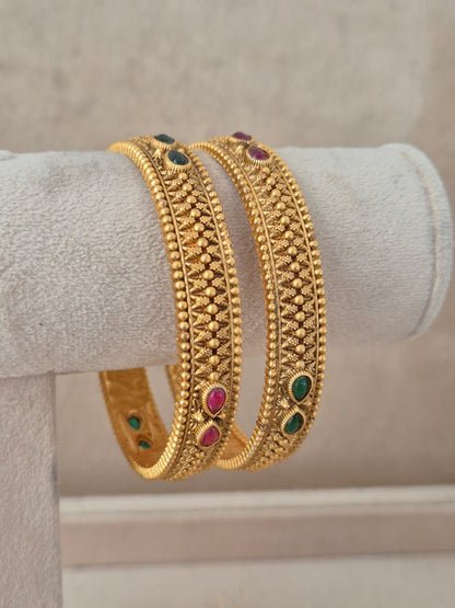 Elegant festive Indian gold-plated bangles with delicate relief work and vibrant gemstone highlights, perfect for weddings, Rakhi, and special occasions by naitri.in