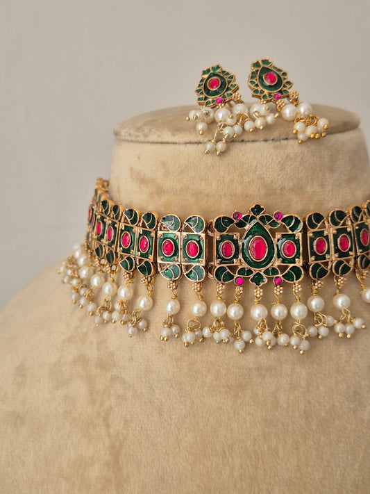 Traditional gold-finish choker necklace featuring alternating green and pink gemstones with a fringe of small white pearls, paired with matching floral stud earrings by naitri.in