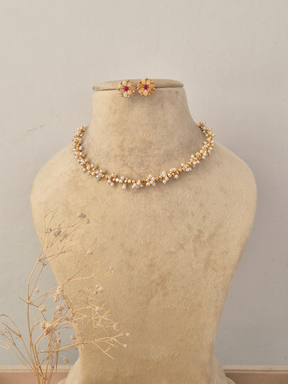 Ruby Necklace Set displayed on a neutral beige mannequin, featuring a delicate golden chain intertwined with vibrant red ruby-like stone accents and matching stud earrings by Naitri.in