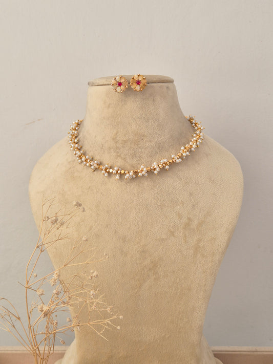 Ruby Necklace Set displayed on a neutral beige mannequin, featuring a delicate golden chain intertwined with vibrant red ruby-like stone accents and matching stud earrings by Naitri.in
