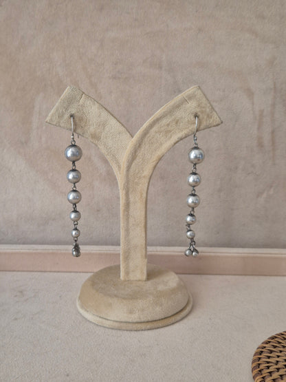 Pair of Sabina silver-toned long dangle earrings featuring a vertical string of polished metallic beads by naitri.in