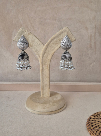 Pair of oxidized silver jhumka earrings with leaf-patterned studs and white pearl drops by naitri.in