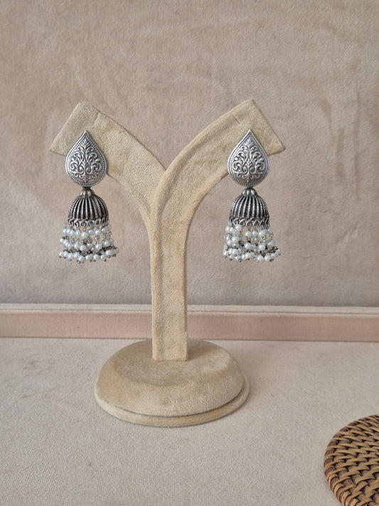 Pair of oxidized silver jhumka earrings with leaf-patterned studs and white pearl drops by naitri.in