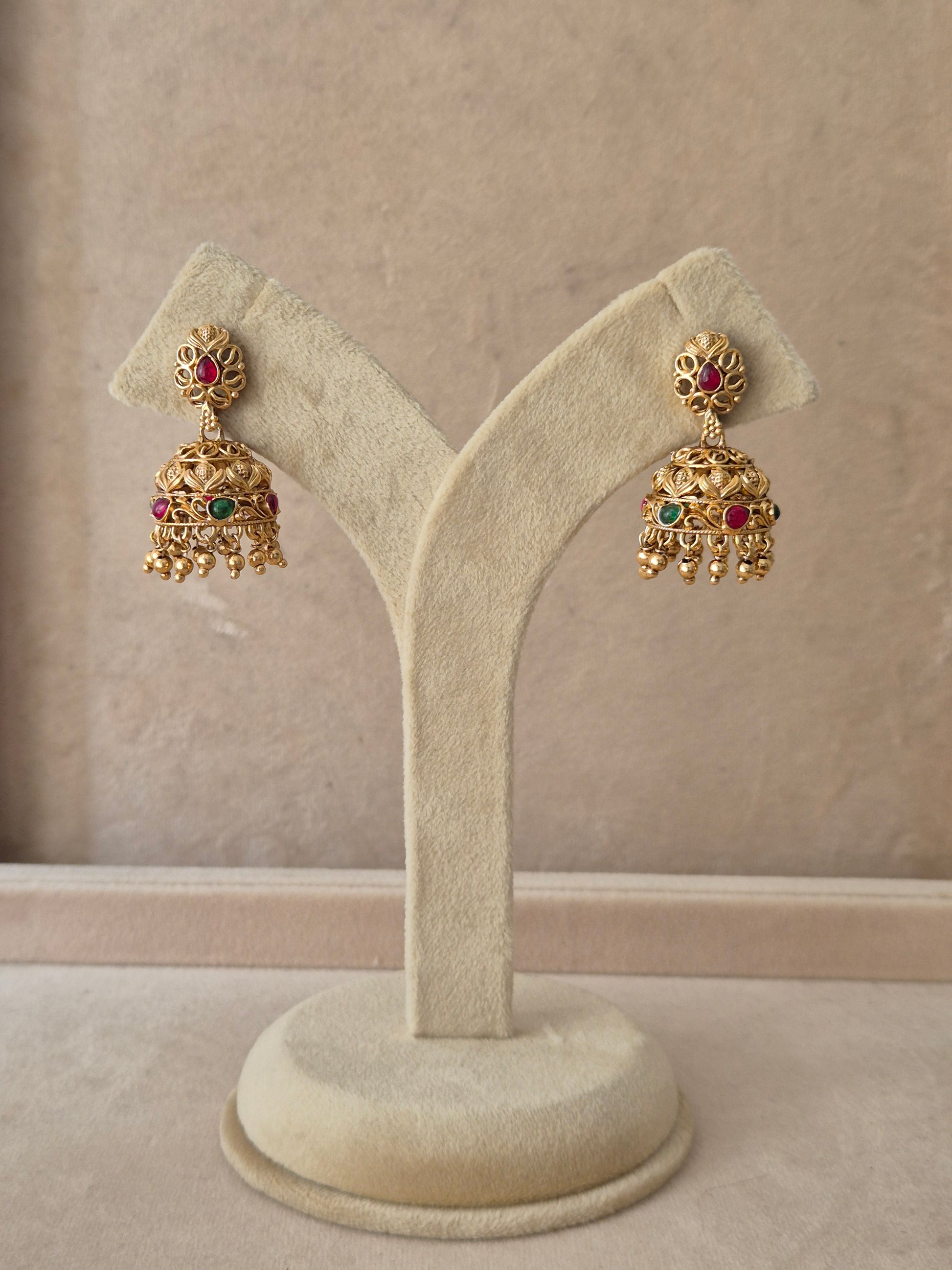 Pair of traditional gold Jhumka earrings with intricate floral detailing, red gemstones, and tiny hanging beads by naitri.in