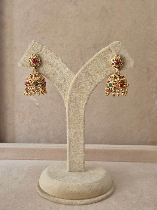 Pair of traditional gold Jhumka earrings with intricate floral detailing, red gemstones, and tiny hanging beads by naitri.in
