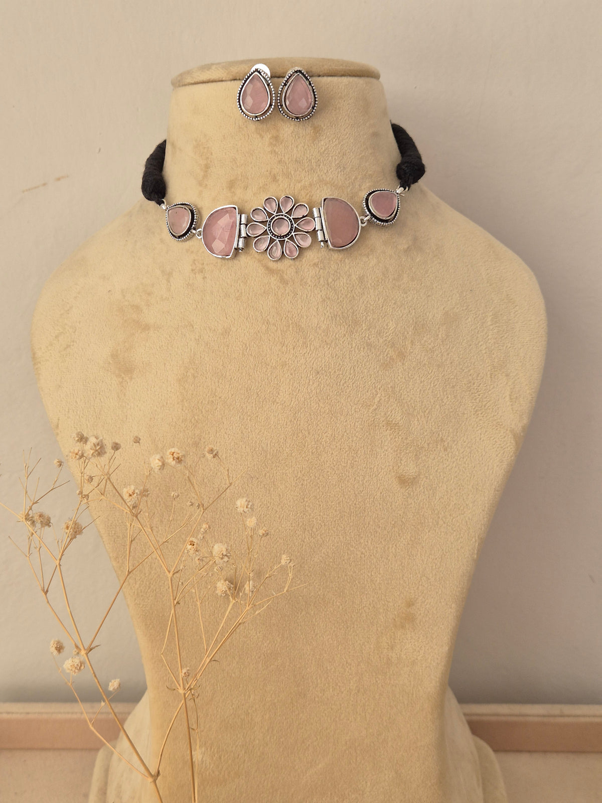 Handcrafted pink stone necklace set displayed on a neutral mannequin, featuring intricate metalwork and matching stud earrings by Naitri.in