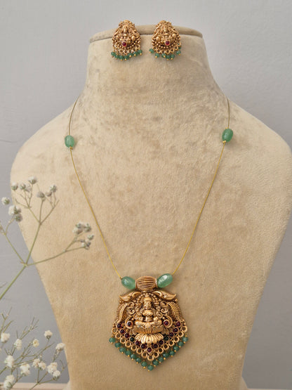 Antique gold-finish Temple jewelry set featuring a pendant with an intricate deity carving, green bead accents, an invisible chain, and matching jhumka-style earrings by naitri.in