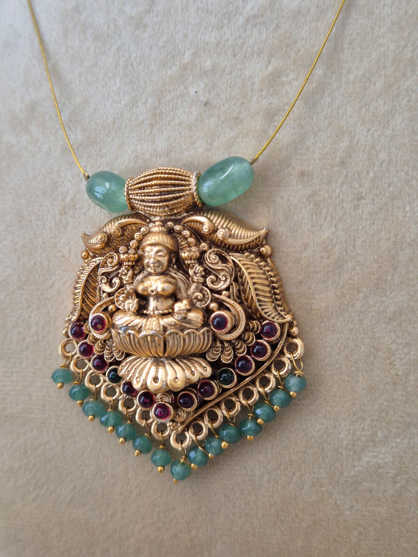 Antique gold-finished Indian temple jewelry pendant with a carved goddess figurine, detailed filigree, hanging pink and green seed beads, and two large light-green barrel beads attached to a fine gold wire chain naitri.in