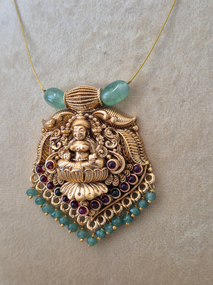 Antique gold-finished Indian temple jewelry pendant with a carved goddess figurine, detailed filigree, hanging pink and green seed beads, and two large light-green barrel beads attached to a fine gold wire chain naitri.in