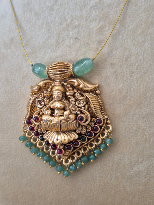 Antique gold-finished Indian temple jewelry pendant with a carved goddess figurine, detailed filigree, hanging pink and green seed beads, and two large light-green barrel beads attached to a fine gold wire chain naitri.in