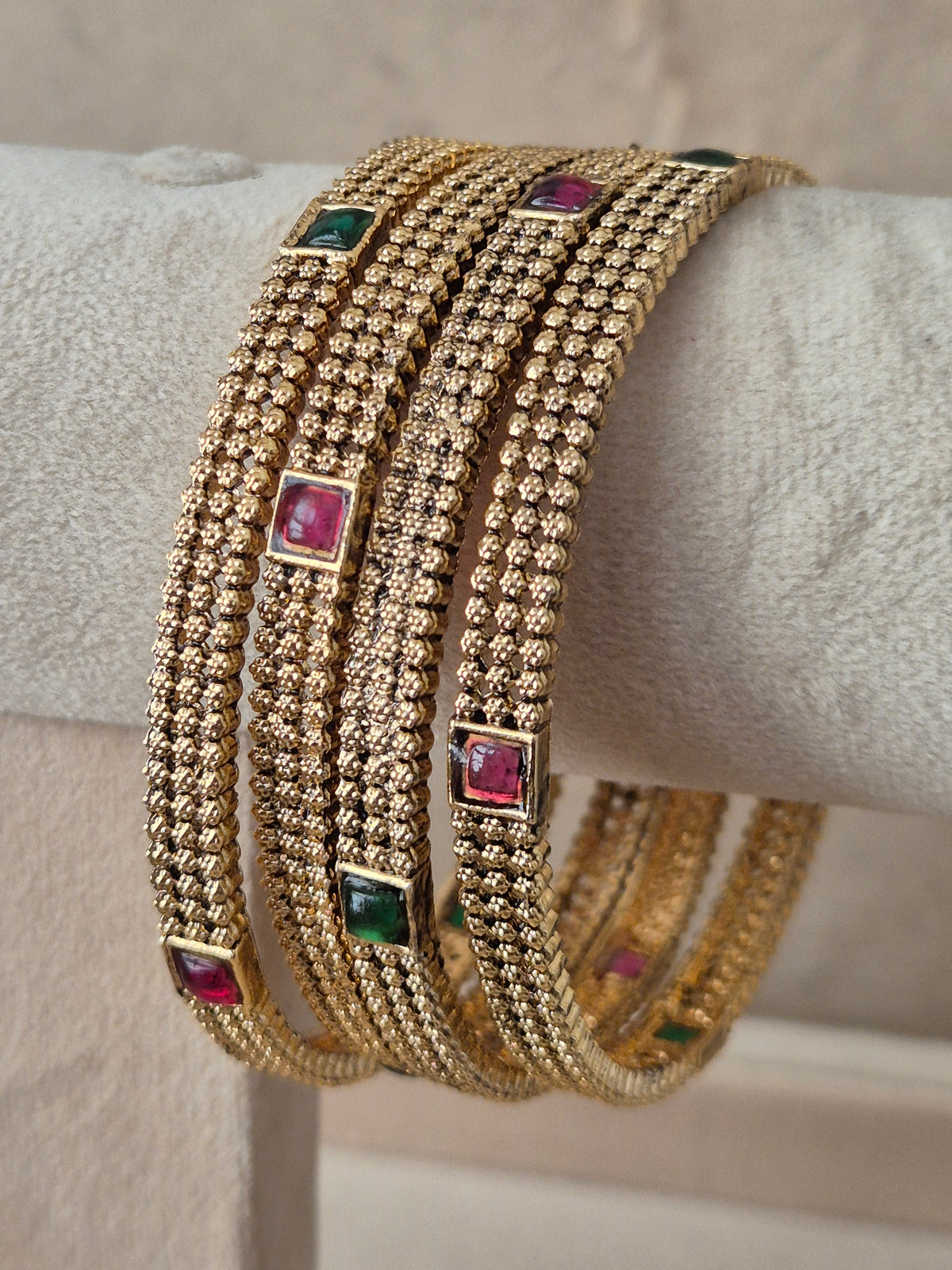 Four traditional gold-plated ethnic bangles with detailed geometric patterns and inlaid red and green gemstones by naitri.in