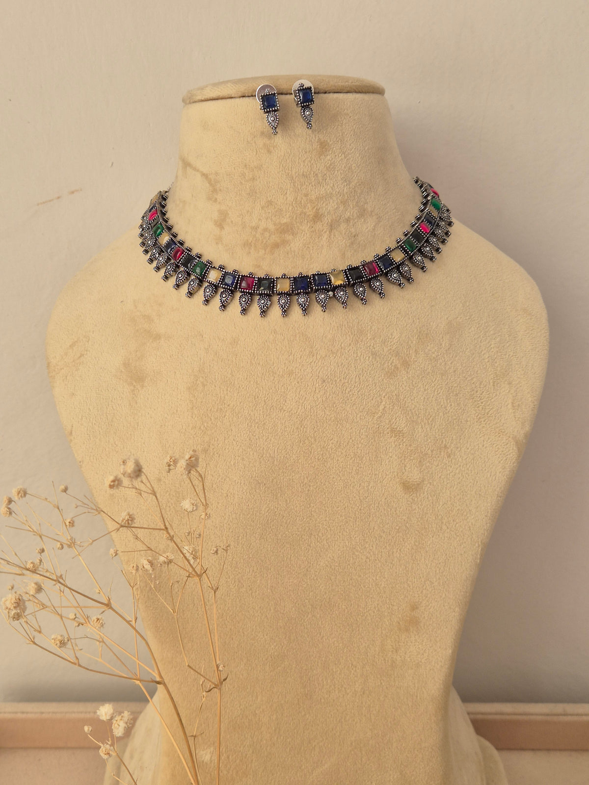 A silver-toned choker necklace and matching drop earrings  The necklace features a row of colorful rectangular gemstones in blue, pink, green, yellow, and red, with dangling silver teardrop-shaped charms by naitri.in