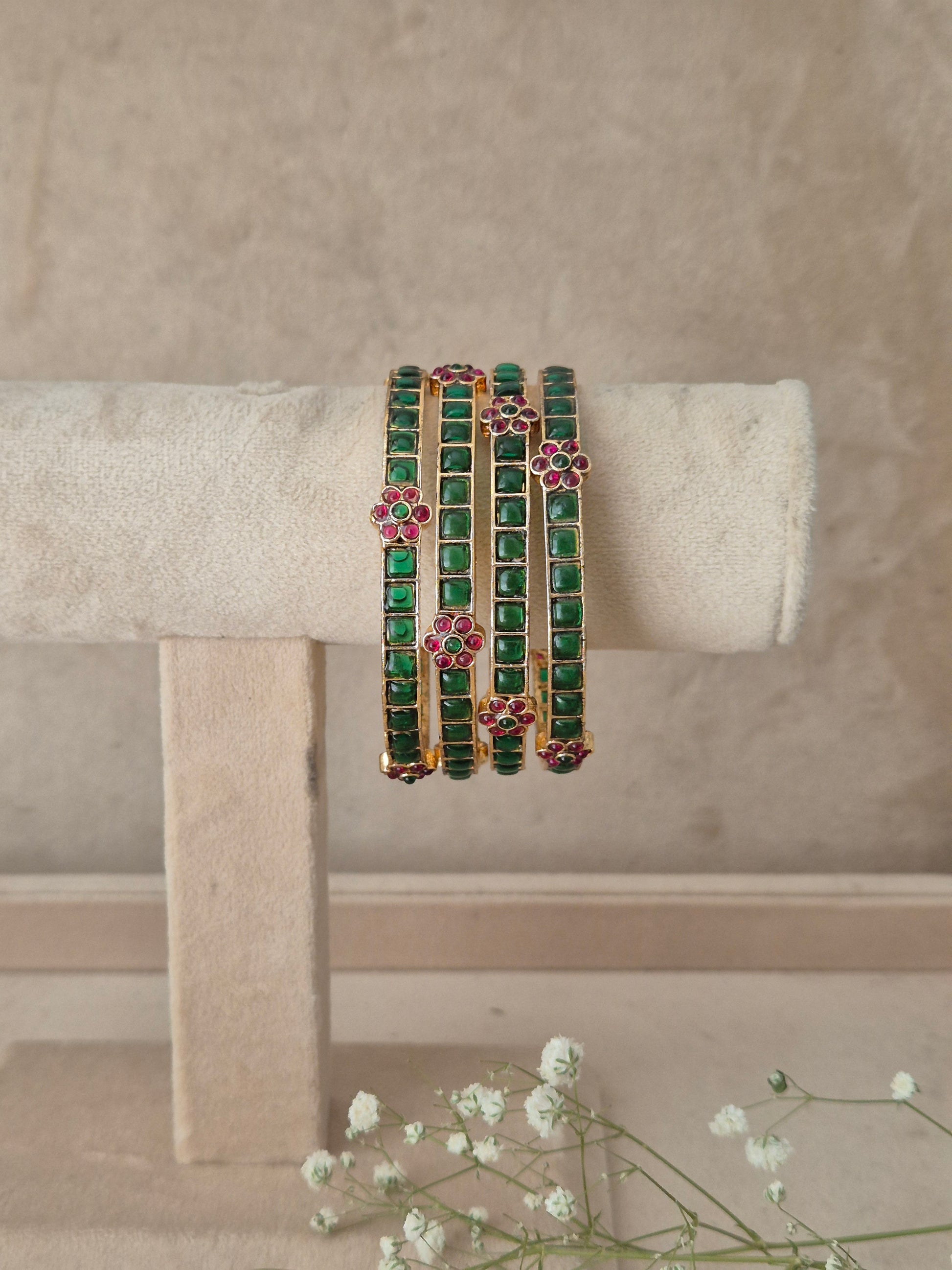 Four gold-plated bangles decorated with green square-cut stones and pink floral accents, by naitri.in