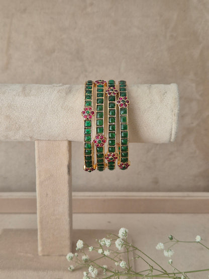 Four gold-plated bangles decorated with green square-cut stones and pink floral accents, by naitri.in