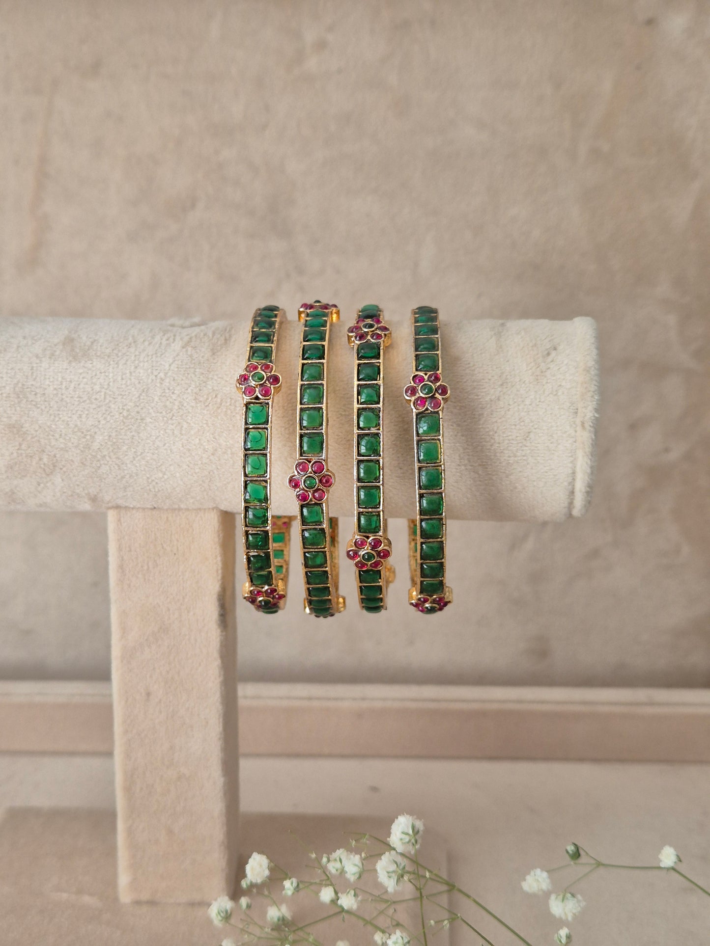 Traditional Indian festive bangles adorned with green gemstones and pink floral stone clusters gold-plated bangles featured with green stone embellishments and pink floral stone detailing by naitri.in