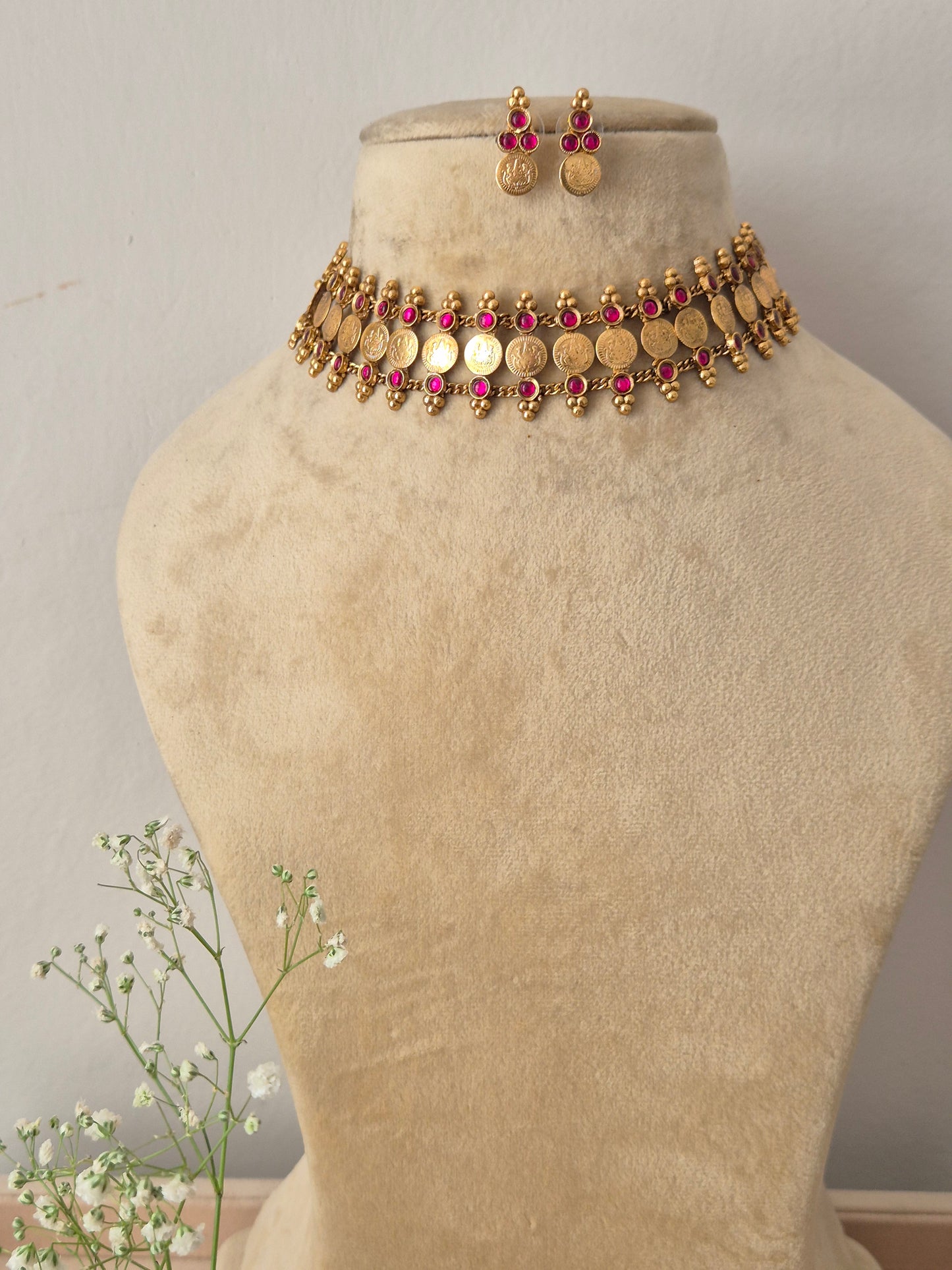 A gold-plated traditional ethnic choker necklace featuring a row of circular coin motifs and hanging red bead droplets, with matching earrings by naitri.in