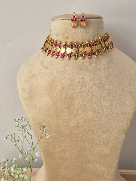 A gold-plated traditional ethnic choker necklace featuring a row of circular coin motifs and hanging red bead droplets, with matching earrings by naitri.in