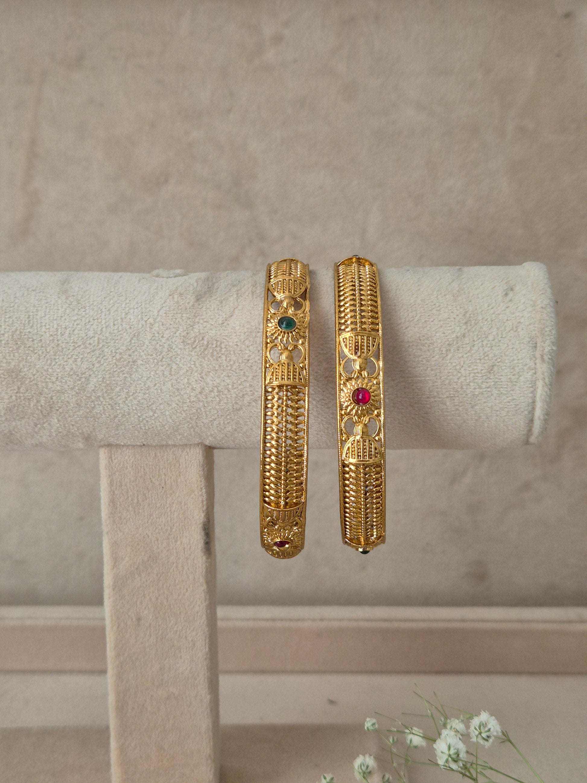Two gold-toned bangles with detailed filigree and small colored stone accents, by naitri.in