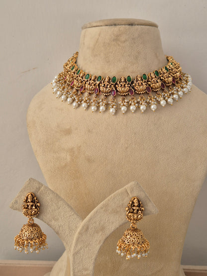 Shreya Necklace Set with matching jhumka earrings in antique gold finish featuring deities, ruby and emerald stones, and pearl drops by naitri.in