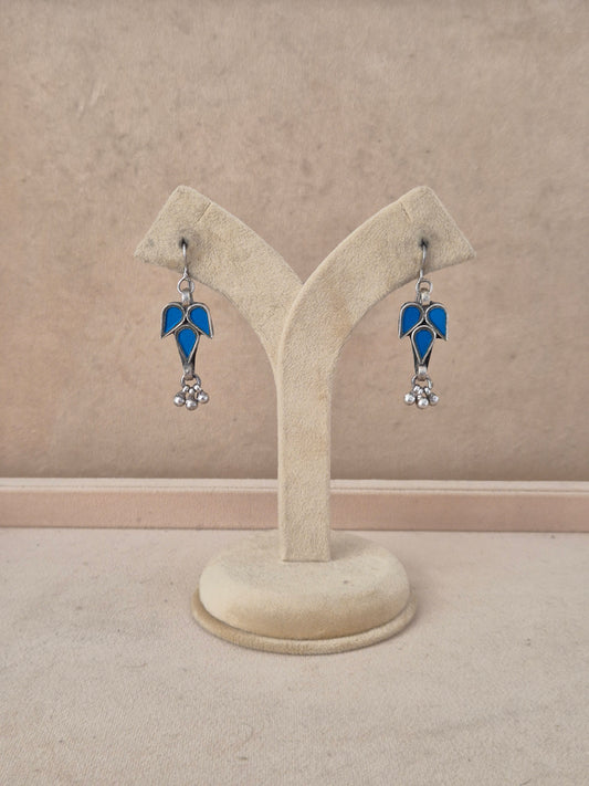 A pair of silver-toned dangle earrings with blue glass leaf-shaped tops and small silver bead drops, by naitri.in