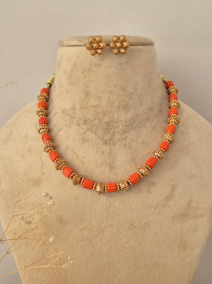 Close-up product view of a gold and orange bead necklace paired with small matching stud earrings