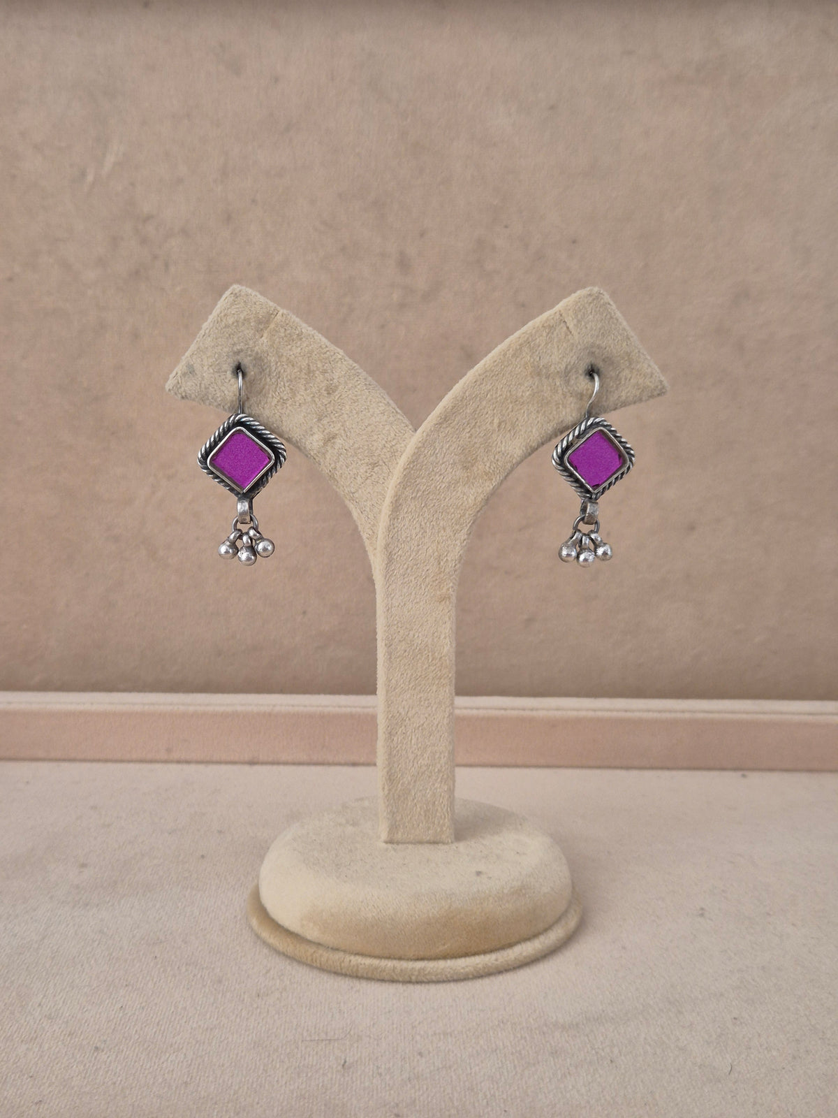 A pair of silver-toned dangle earrings with bright purple square stones and small clear crystal drops, by naitri.in