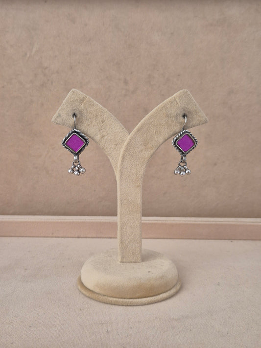 A pair of silver-toned dangle earrings with bright purple square stones and small clear crystal drops, by naitri.in