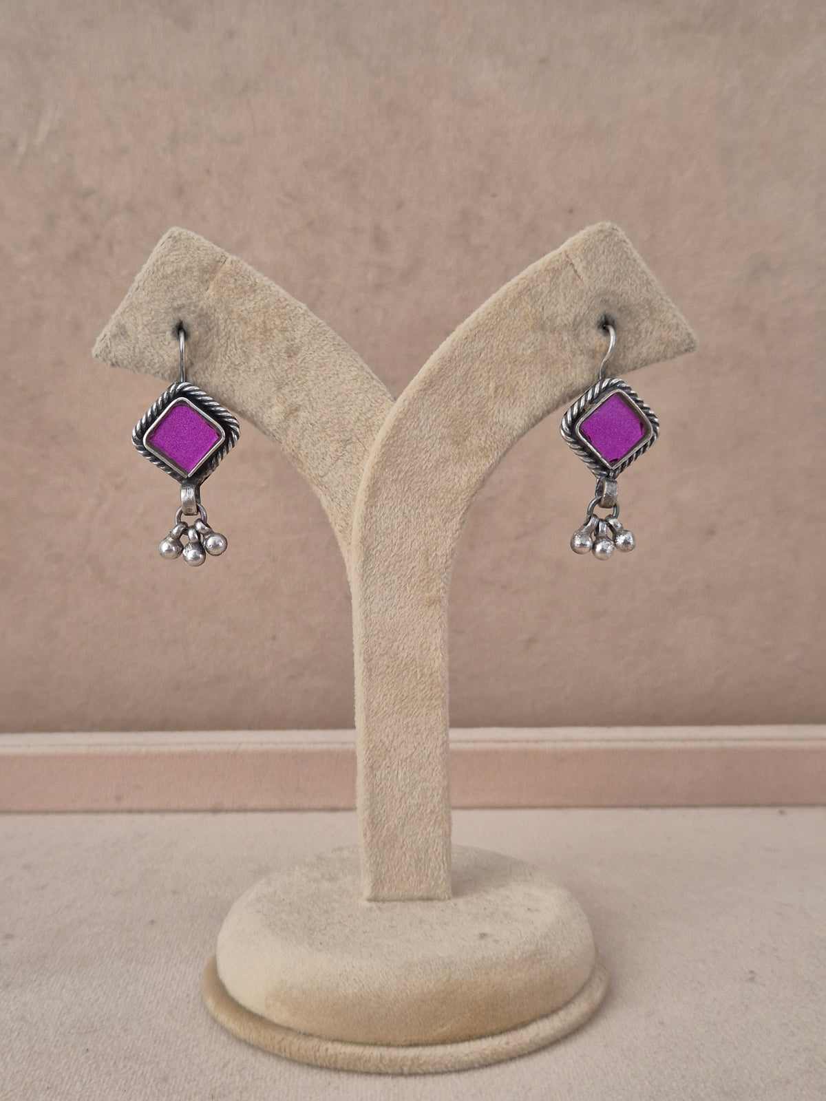 A pair of silver-toned dangle earrings with bright purple square stones, by naitri.in
