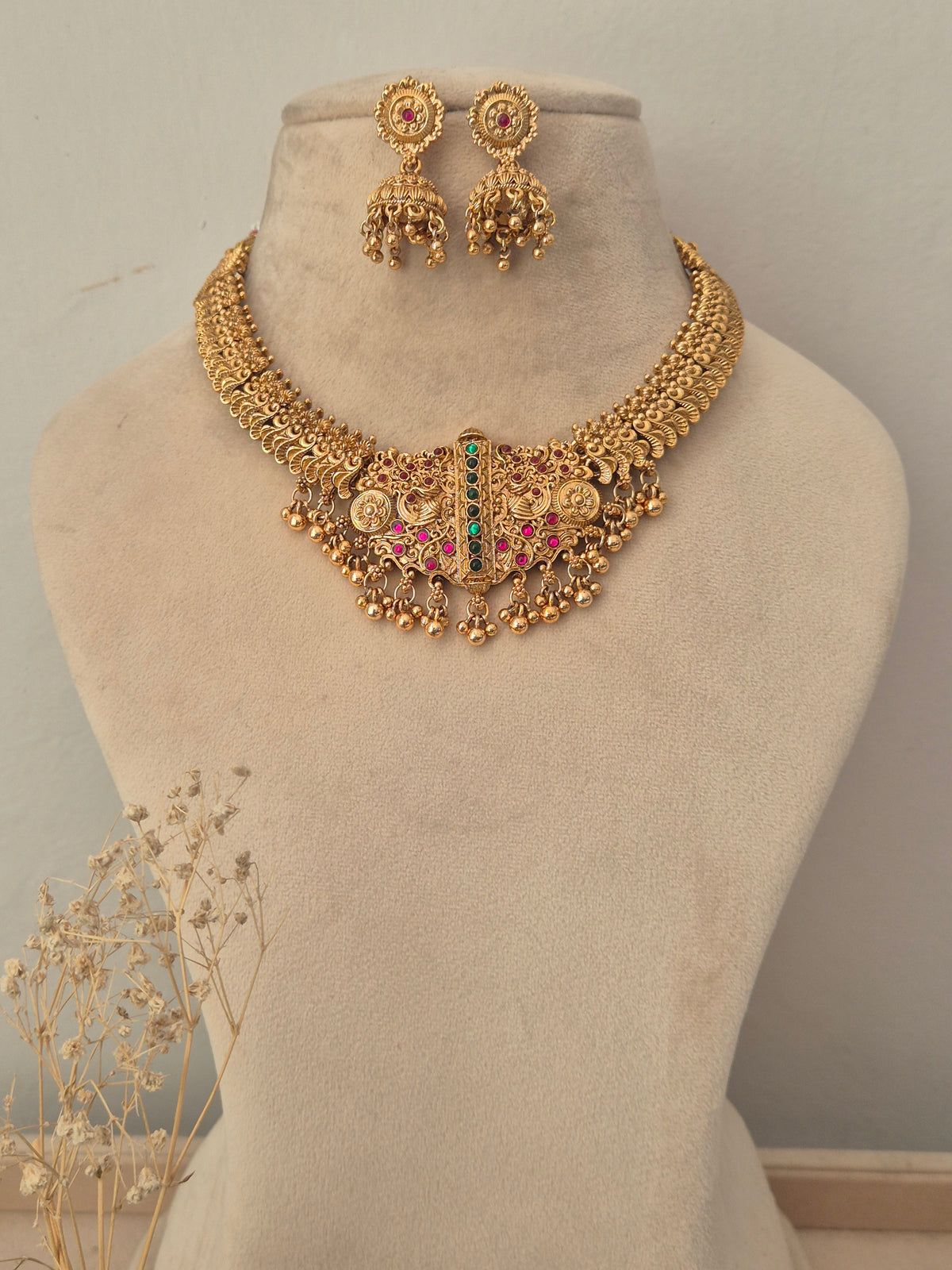 Gold-toned traditional jewelry set including a statement necklace with dangling coins, beads, and a central green and pink stone accent, plus matching earrings by naitri.in