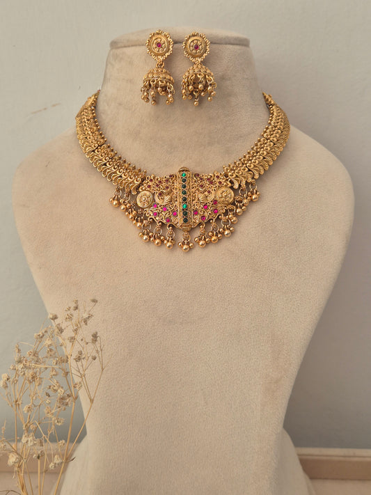 Gold-toned traditional jewelry set including a statement necklace with dangling coins, beads, and a central green and pink stone accent, plus matching earrings by naitri.in
